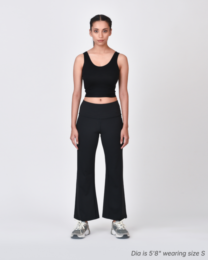 Woman wearing a black tank top and black flare pants on a white background